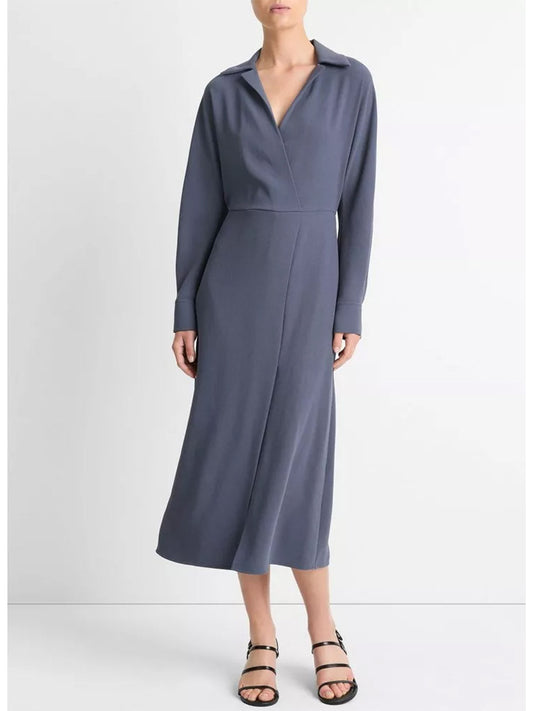 A person styled in the Vince Shaped Collar Dolman-Sleeve Dress in Dark Water, a long-sleeve, knee-length dress featuring an elasticized waist, pairs it with black sandals and stands against a plain white background.