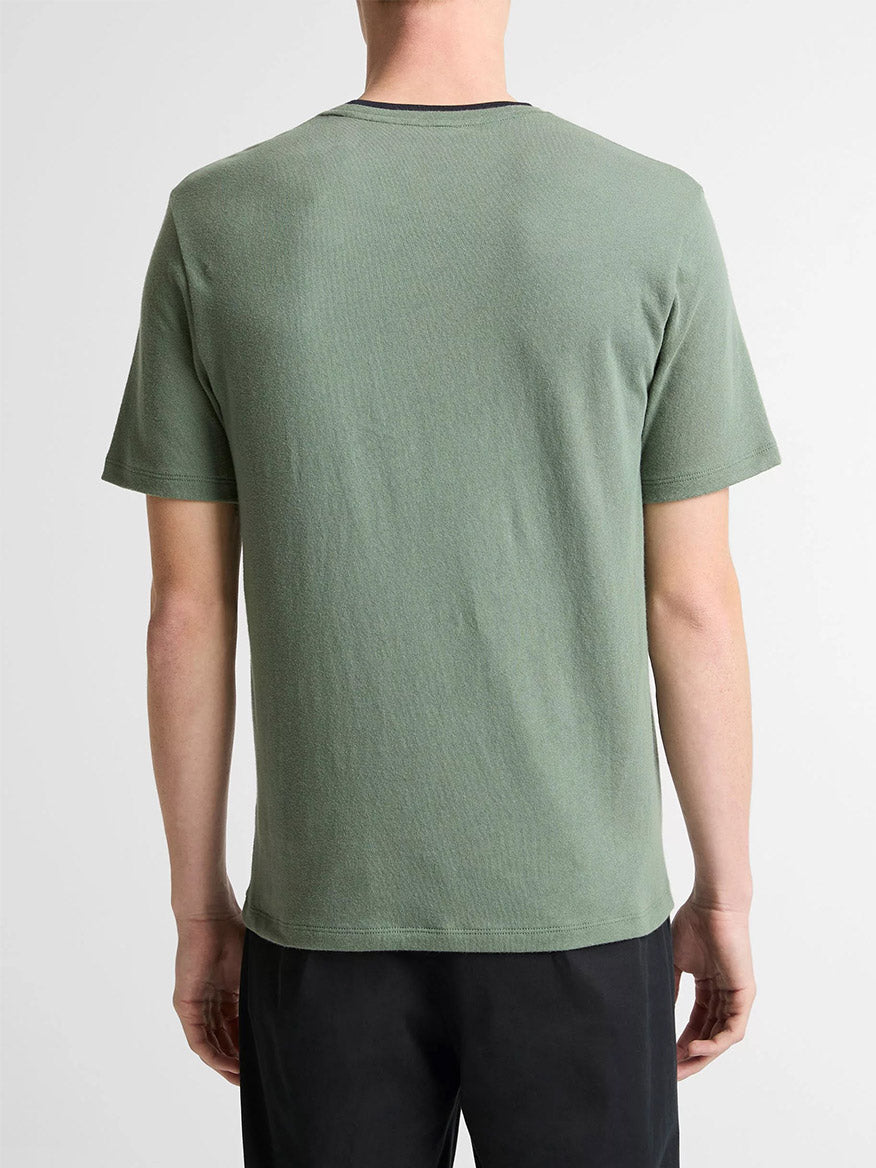 A person stands with their back to the camera, wearing the Vince Cotton Double-Collar T-Shirt in Laurel/Coastal Blue and black pants against a plain light background.