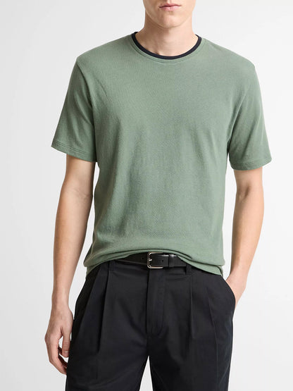 A person wearing the Vince Cotton Double-Collar T-Shirt in Laurel/Coastal Blue and black pleated pants stands with one hand in a pocket.