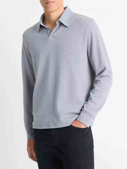 A person wearing a Blue Spruce/Light Grey Vince Double Face long-sleeve polo shirt and black pants stands with one hand in their pocket. Their head is not visible.