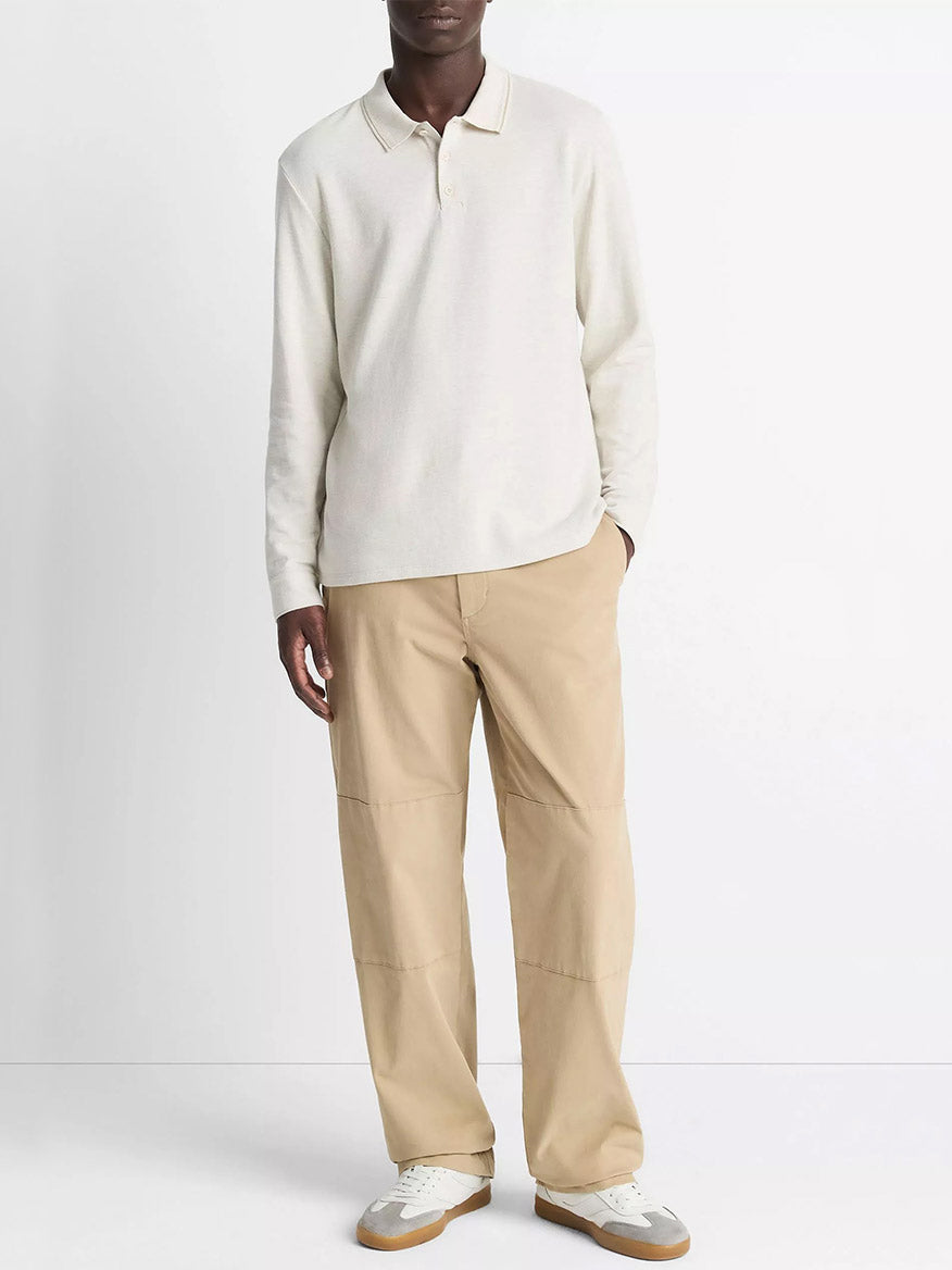 A person stands against a plain background wearing the Vince Heathered Double-Face Cotton-Blend Polo Shirt in Heather Blanco/Terrapin, tan pants, and white sneakers.