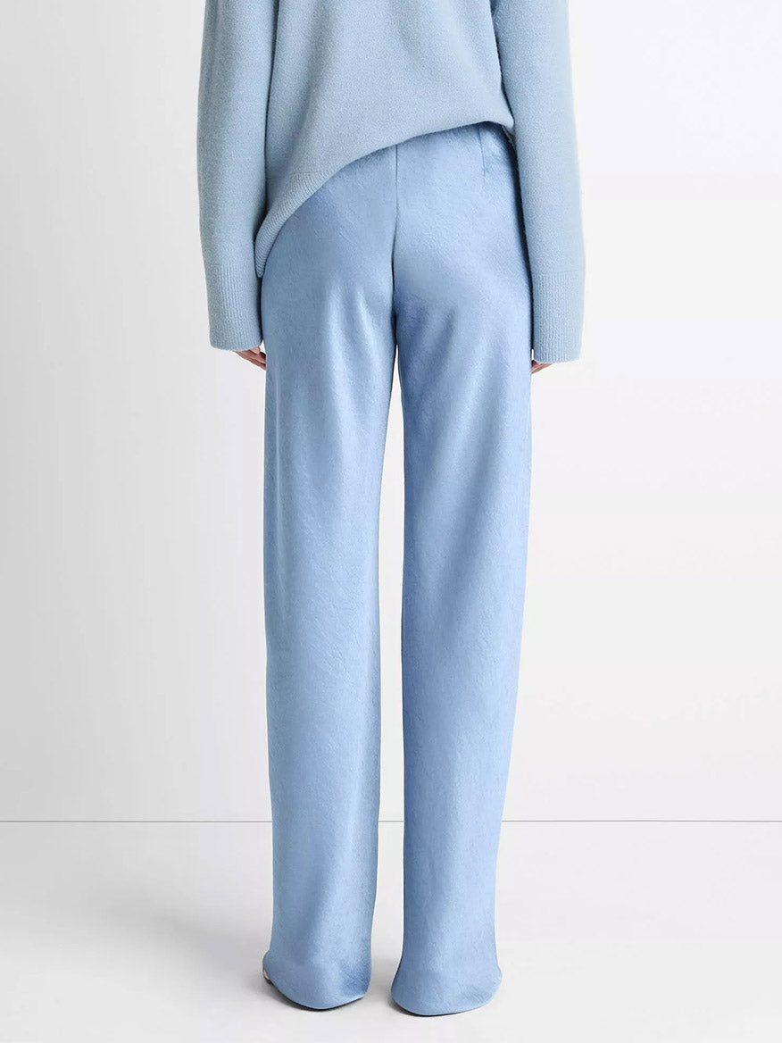 Someone is seen from behind against a plain light background, wearing the Vince Fluid Satin Bias Pant in Pacific paired with a matching light blue sweater.