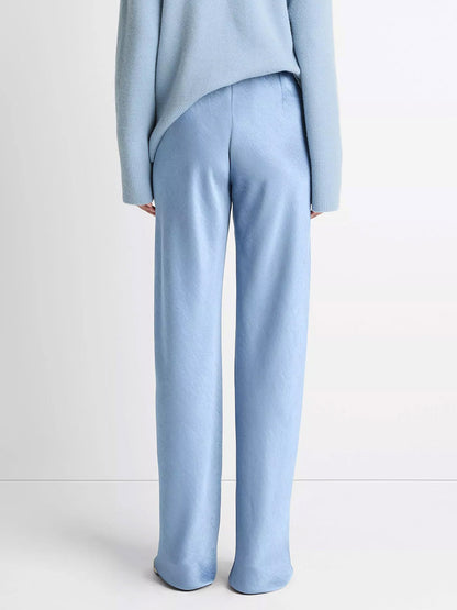 Someone is seen from behind against a plain light background, wearing the Vince Fluid Satin Bias Pant in Pacific paired with a matching light blue sweater.
