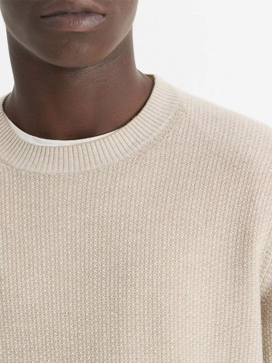 A person wearing the Vince Geo-Jacquard Wool-Blend Crew Neck Sweater in British Khaki/Classic Cream layered over a white shirt. The photo showcases the lower half of their face and upper chest against a simple backdrop.