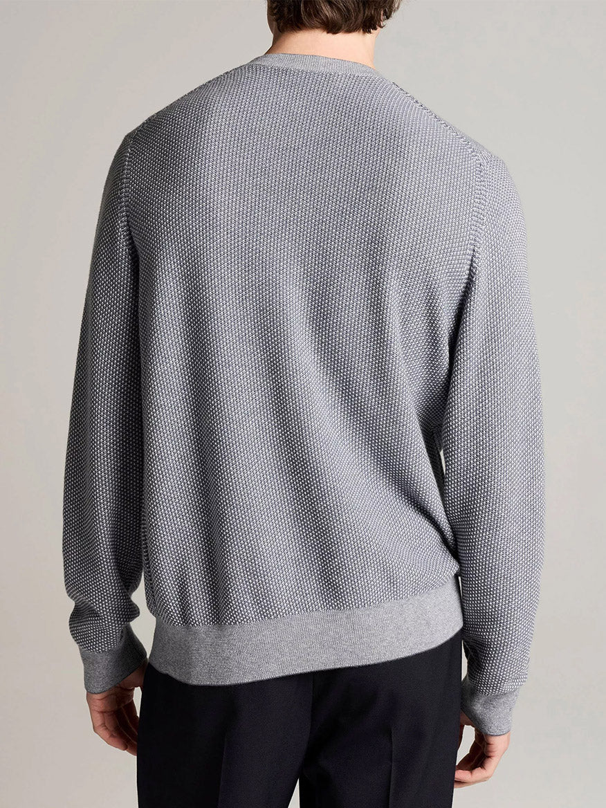 Wearing the Vince Geo-Jacquard Wool-Blend Crew Neck Sweater in Late Evening/Classic Cream—a textured light gray knit crafted from a wool-cotton-cashmere blend—and black pants, the person is shown from the back against a plain background.