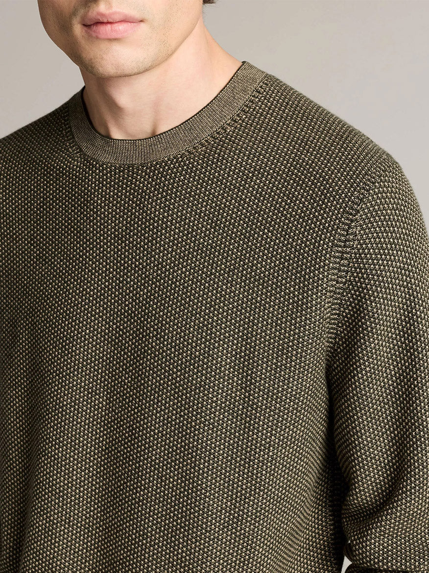 A person wears the Vince Geo-Jacquard Wool-Blend Crew Neck Sweater in Midnight Garden/River Sand, crafted from a luxurious blend of wool, cotton, and cashmere. The image is cropped at the mouth, shoulders, and mid-arm to highlight the sweater’s intricate jacquard pattern.