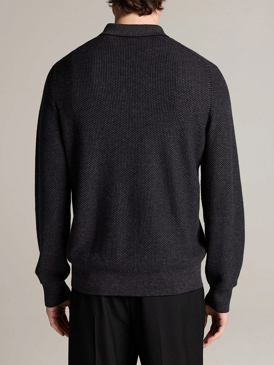 A man is standing with his back to the camera, wearing the Vince Geo-Jacquard Wool-Blend Zip Polo Sweater in Coastal Blue/Medium Heather Grey and black pants against a plain background.