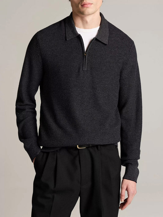 A man wearing the Vince Geo-Jacquard Wool-Blend Zip Polo Sweater in Coastal Blue/Medium Heather Grey over a white t-shirt, paired with black pleated trousers and a black belt, stands against a plain background.