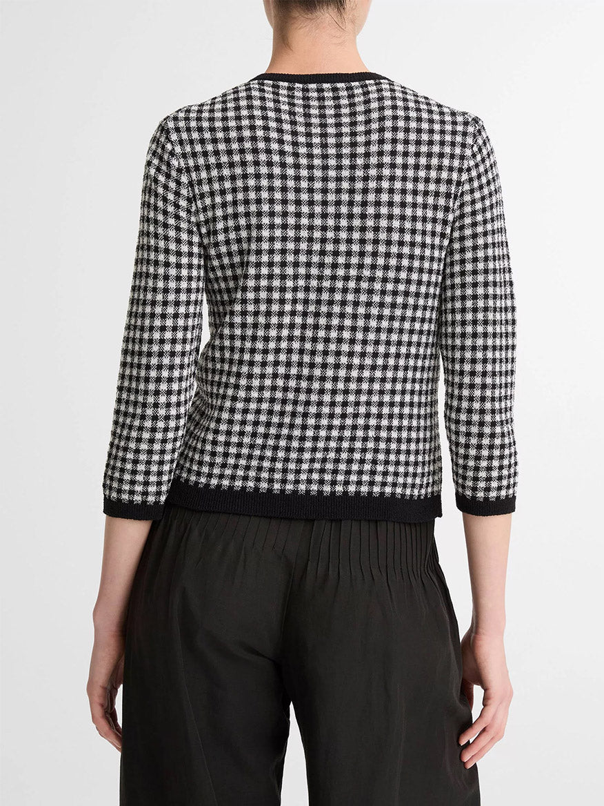 A person is shown from behind, wearing the Vince Gingham Italian Wool Blend Cardigan in Black/Off-White with three-quarter sleeves and black pants. Its wool-cotton blend offers transitional weight comfort, set against a plain backdrop.