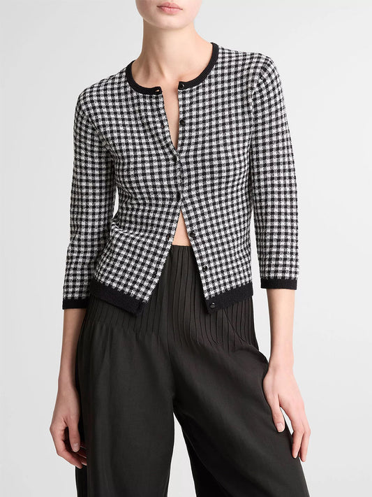 A person wears the Vince Gingham Italian Wool Blend Cardigan in Black/Off-White with black trim and three-quarter sleeves, paired with high-waisted, pleated black pants. The cardigan offers a stylish blend of wool and cotton for comfort.