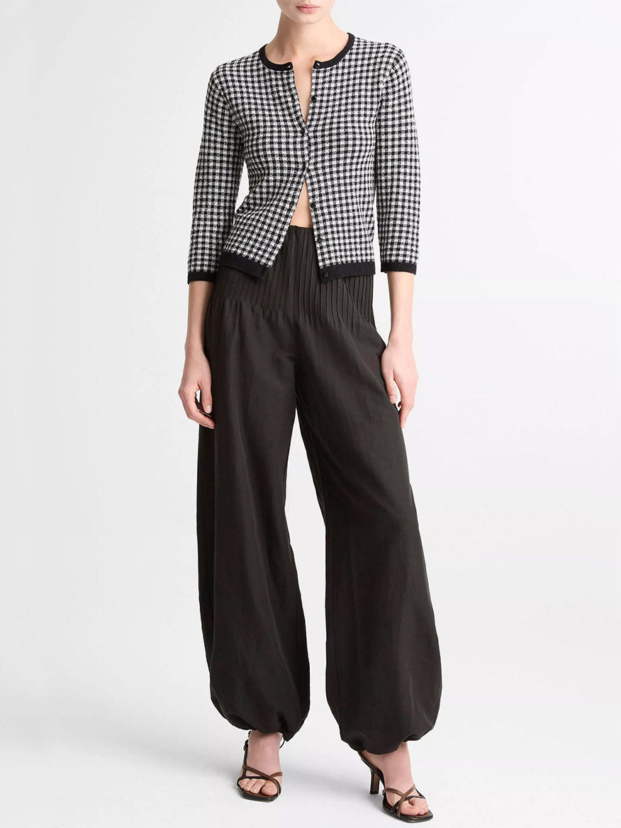 A person wearing the Vince Gingham Italian Wool Blend Cardigan in Black/Off-White, loose high-waisted black pants, and black heeled sandals stands against a plain white background.