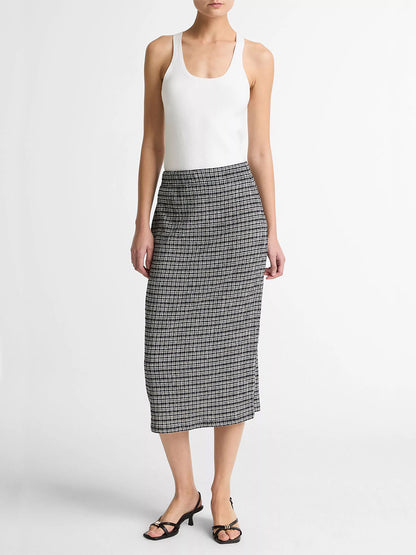 A woman stands against a plain background wearing a white sleeveless top, black heeled sandals, and the Vince Plaid Grid-Knit Midi Skirt in Eclipse Combo.