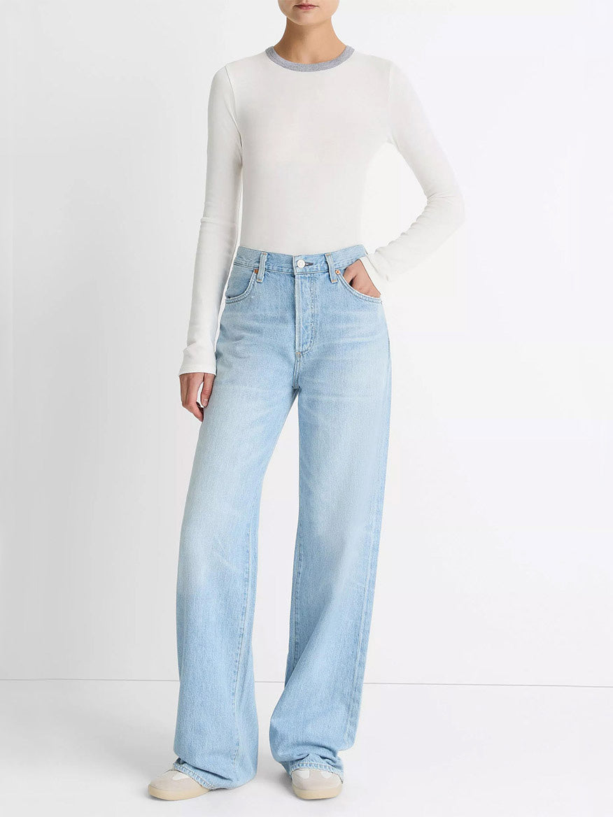A person wears the Vince Tipped Heathered Pima Cotton-Blend Long-Sleeve T-Shirt in Off White Combo, paired with light blue high-waisted wide-leg jeans and white shoes, standing against a plain white background.