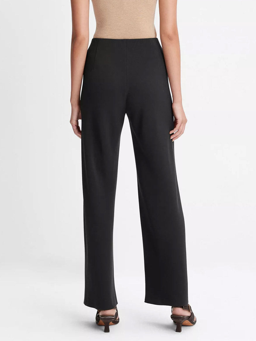 A person wearing Vince High-Waist Crepe Bias Pant in Black, styled with open-toe sandals, is shown from the back against a plain background.
