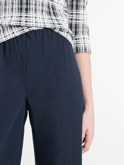 A person in a black and white plaid top pairs it with Vince Cotton-Blend High-Waist Bias Pants in Coastal Blue, sporting an elasticized waist. Their relaxed right arm adds to their effortless style.