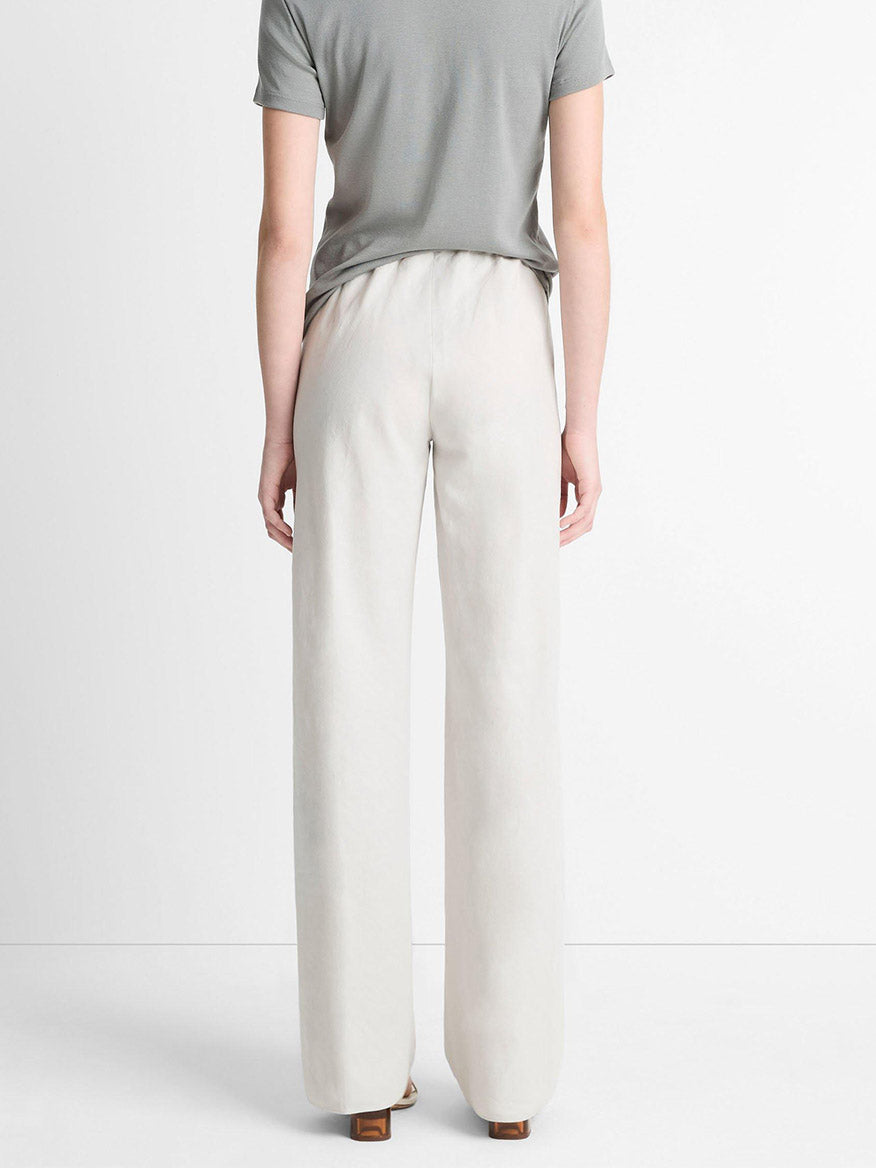 A person is seen from behind in a gray short-sleeved top and Vince Cotton-Blend High-Waist Bias Pant in Salt Glass, featuring an elasticized waist for easy style, against a plain white background.