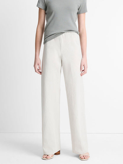 A person in a gray short-sleeve shirt and Vince Cotton-Blend High-Waist Bias Pant in Salt Glass, featuring an elasticized waist, stands against a plain white background.