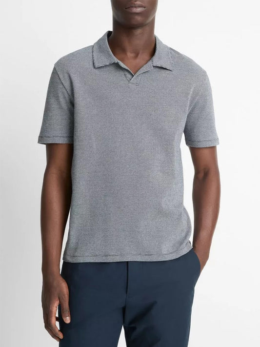 A person in a coastal blue/optic white Vince Houndstooth Pima cotton Johnny-collar polo shirt and dark pants stands with one hand in their pocket.