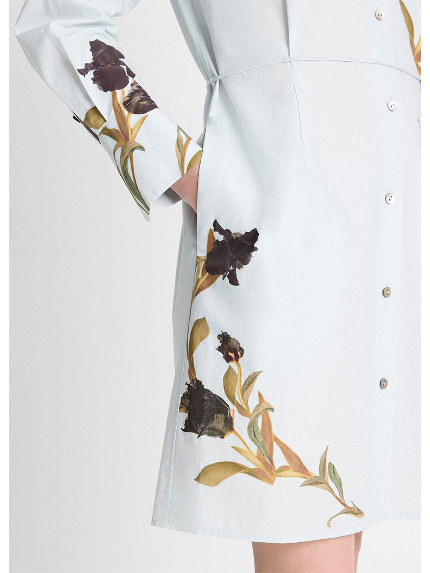 The Vince Placed Iris Cotton Shirt Dress in Salt Glass/Black Iris is a light blue cotton poplin with black and brown floral prints, evoking irises. It features long sleeves, front buttons, and a chic self-tie belt for a customizable fit.