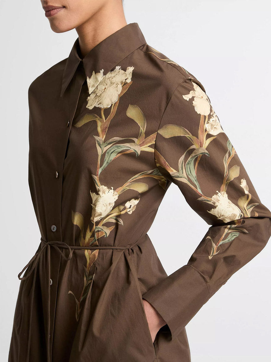 Someone wearing the Vince Placed Iris Cotton Shirt Dress in Dark Bark—a brown cotton dress with long sleeves and iris floral prints on the chest and sleeves.