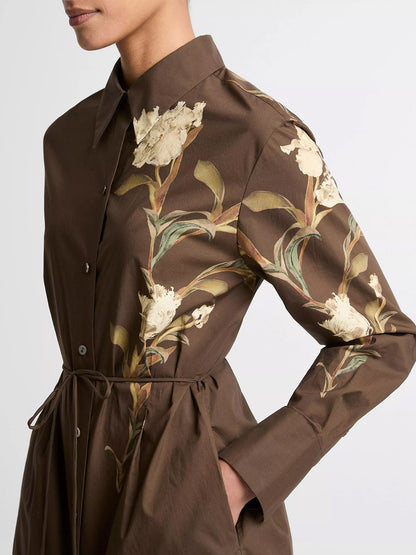 Someone wearing the Vince Placed Iris Cotton Shirt Dress in Dark Bark—a brown cotton dress with long sleeves and iris floral prints on the chest and sleeves.