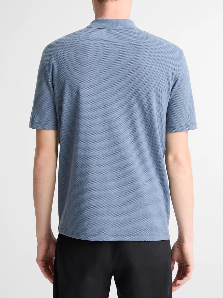 A person is seen from the back wearing a Vince Johnny Collar Polo Shirt in Uniform Blue with mesh construction and black pants, set against a plain background.