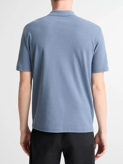 A person is seen from the back wearing a Vince Johnny Collar Polo Shirt in Uniform Blue with mesh construction and black pants, set against a plain background.