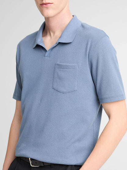 A person wearing the Vince Johnny Collar Polo Shirt in Uniform Blue with black pants stands against a plain background.