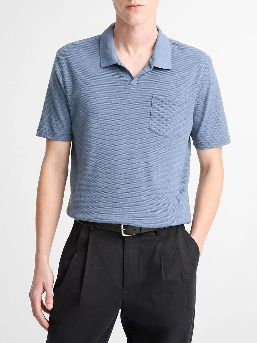 A person is wearing the Vince Johnny Collar Polo Shirt in Uniform Blue, tucked into black trousers with a belt, standing against a plain background.