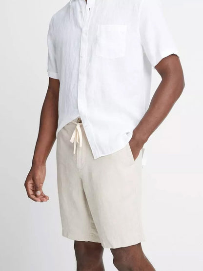 A person wearing a Vince Lightweight Hemp Short in Pumice Rock and beige pull-on shorts with a drawstring closure stands with a hand at their side.