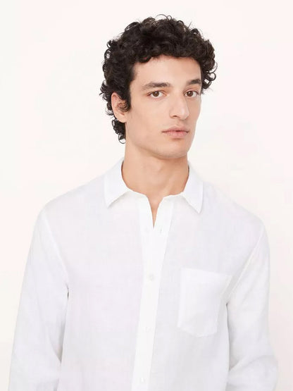 A man with curly hair wearing a Vince Linen Long Sleeve Shirt in Optic White made of cooling linen with a collar and a front pocket.