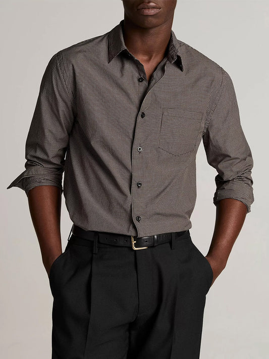 A man wearing the Vince McDermott Plaid Cotton Button-Front Shirt in Arabica/Headline Grey, crafted from cotton poplin, paired with black trousers, stands facing forward with his hands in his pockets against a plain background.