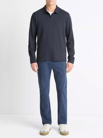 A man stands against a plain background wearing the Vince Milano Pima Cotton-Blend Johnny-Collar Shirt in Coastal Blue, blue pants, and white sneakers.