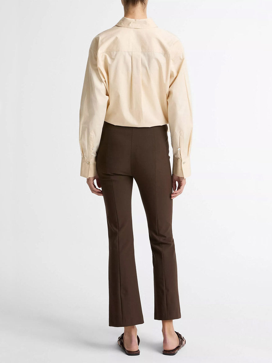 A person faces away, wearing a cream long-sleeve shirt and Vince Niki Mid-Rise Pintuck Crop Flare Pant in Willow, made from Italian cotton-blend bi-stretch fabric, paired with sandals against a plain white background.