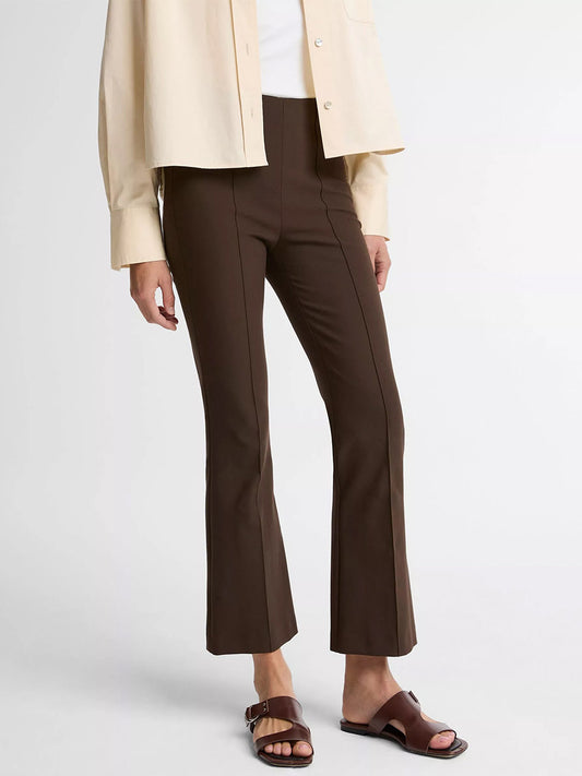 A woman wears the Vince Niki Mid-Rise Pintuck Crop Flare Pant in Willow, paired with a cream button-up shirt, white top, and brown slide sandals, standing against a plain white background.