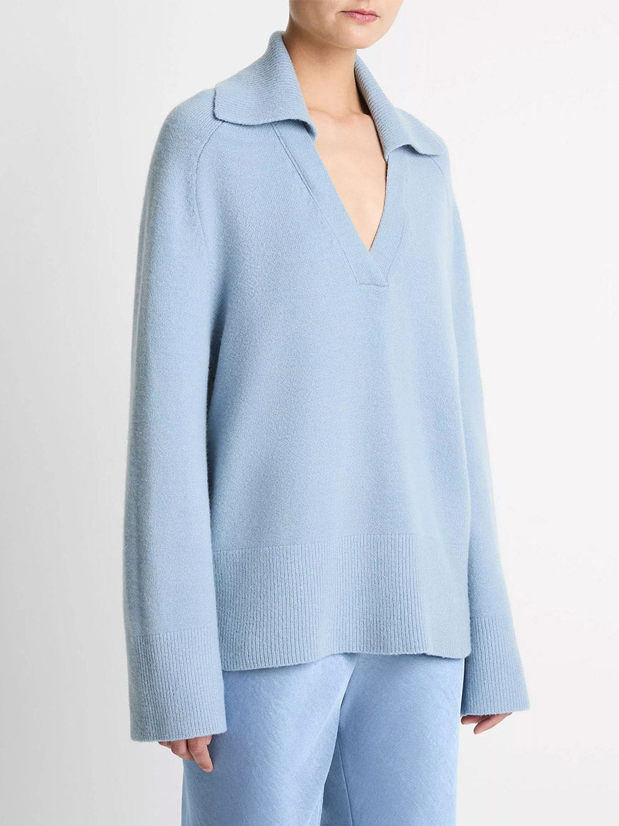 A person wears the Vince Wool & Cashmere-Blend Oversized Polo Sweater in Pacific, featuring a wide collar and deep V-neck, elegantly paired with matching light blue pants.