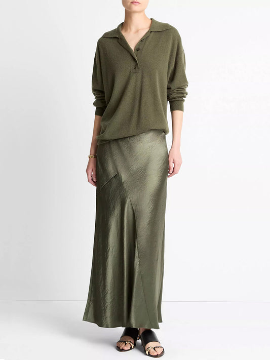 A person wearing an olive green long-sleeve top, the Vince Paneled Satin Bias Skirt in Herba, and black sandals, standing against a plain white background.