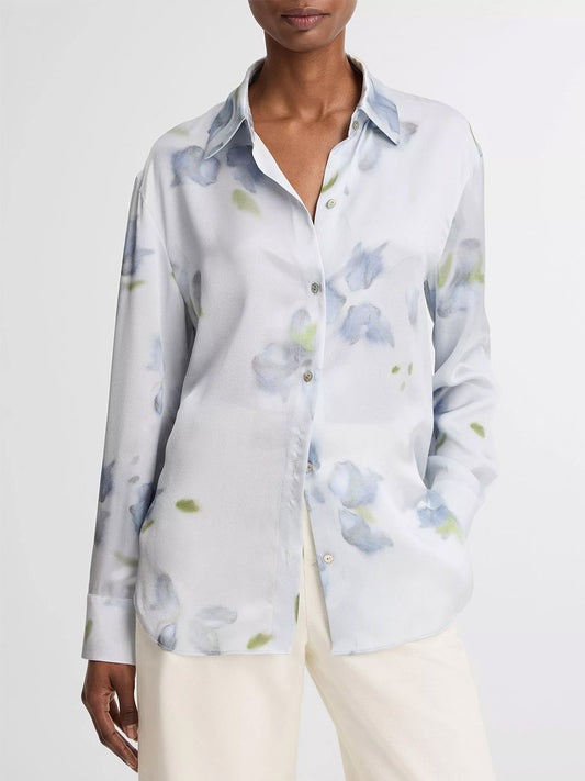 A person wearing the Vince Petal Blur Silk Relaxed Button-Front Shirt in Soft Grey, featuring a blue and green floral print, paired with light pants.
