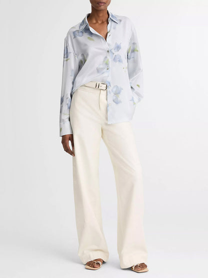 A person wears the Vince Petal Blur Silk Relaxed Button-Front Shirt in Soft Grey, paired with cream wide-leg belted pants and open-toe sandals, standing against a plain background.