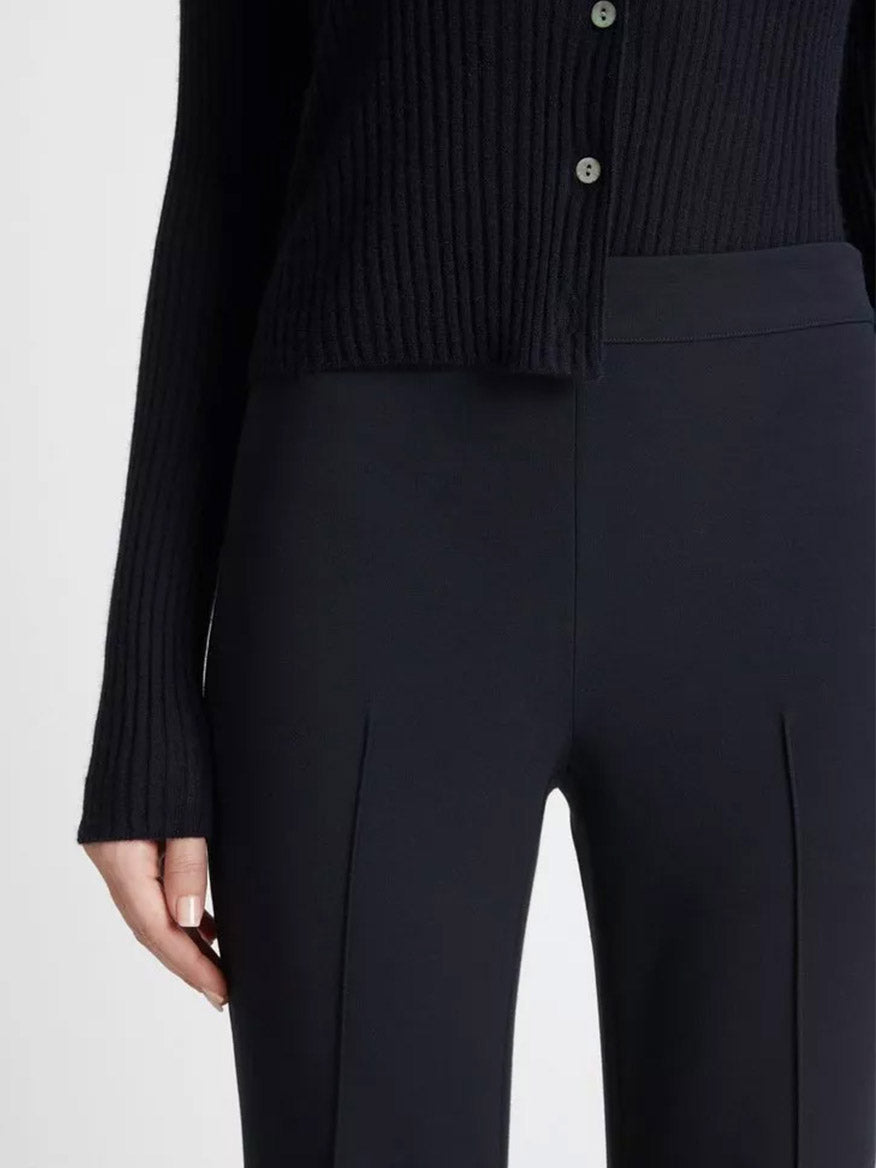Close-up of a person wearing a black ribbed sweater made from Italian cotton and Vince Mid-Rise Pintuck Crop Flare Pant in Coastal Blue, focusing on the midsection and showing the fabric details and button design.