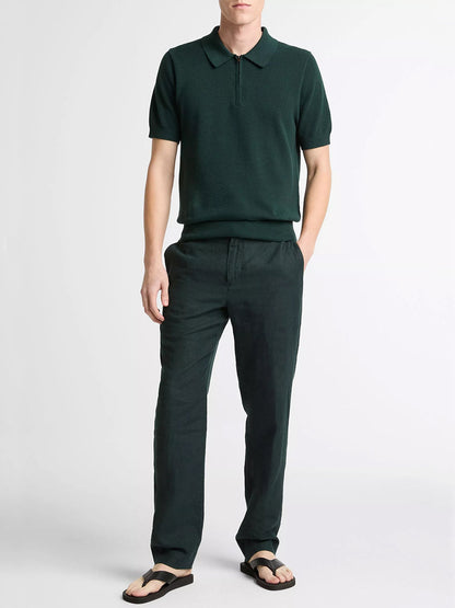 A person stands against a plain background wearing the Vince Cotton-Cashmere Piqué Zip Polo Sweater in Seaweed, matching green pants, and black flip-flops.