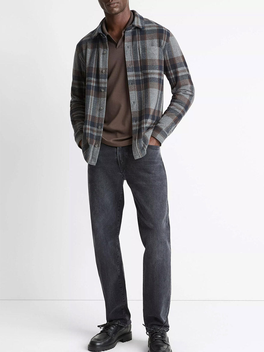 A man stands against a plain white background wearing the Vince Plaid Cotton-Blend Shirt Jacket in Medium Heather Grey Combo over a brown t-shirt, paired with dark jeans and black shoes.