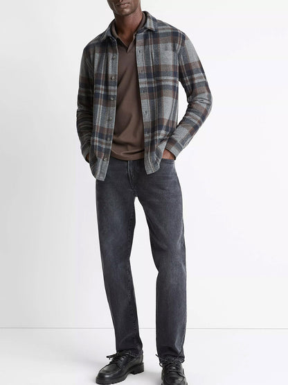 A man stands against a plain white background wearing the Vince Plaid Cotton-Blend Shirt Jacket in Medium Heather Grey Combo over a brown t-shirt, paired with dark jeans and black shoes.