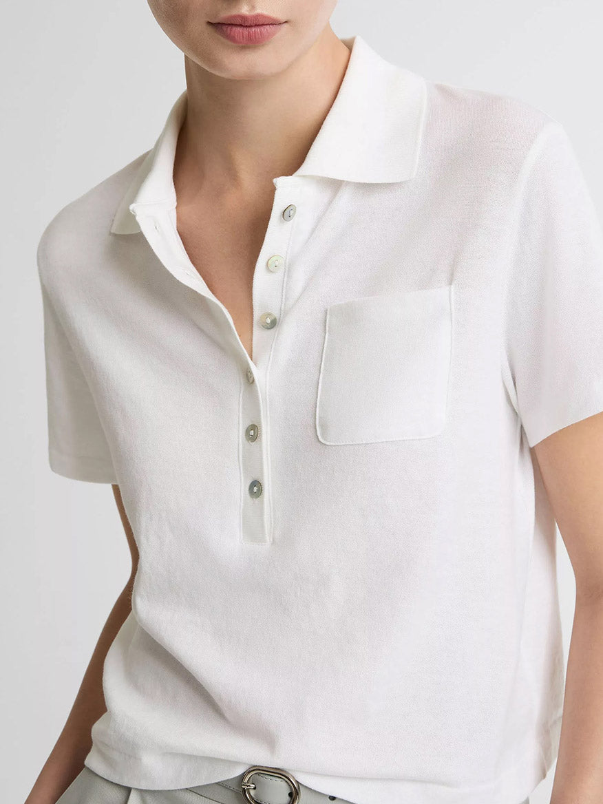A person wears the Vince Cotton Cropped Pocket Polo in Optic White—a boxy, lightweight cotton shirt with a chest pocket and agoya shell buttons. The photo is cropped at the nose and mid-waist.