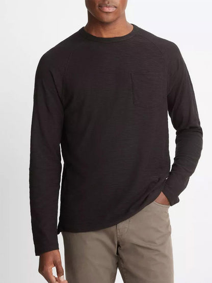 Dressed in a Vince Cotton Long Sleeve Pocket Crew T-Shirt in black, crafted from soft Peruvian cotton and featuring a small chest pocket, an individual pairs it with khaki pants while standing against a plain background.