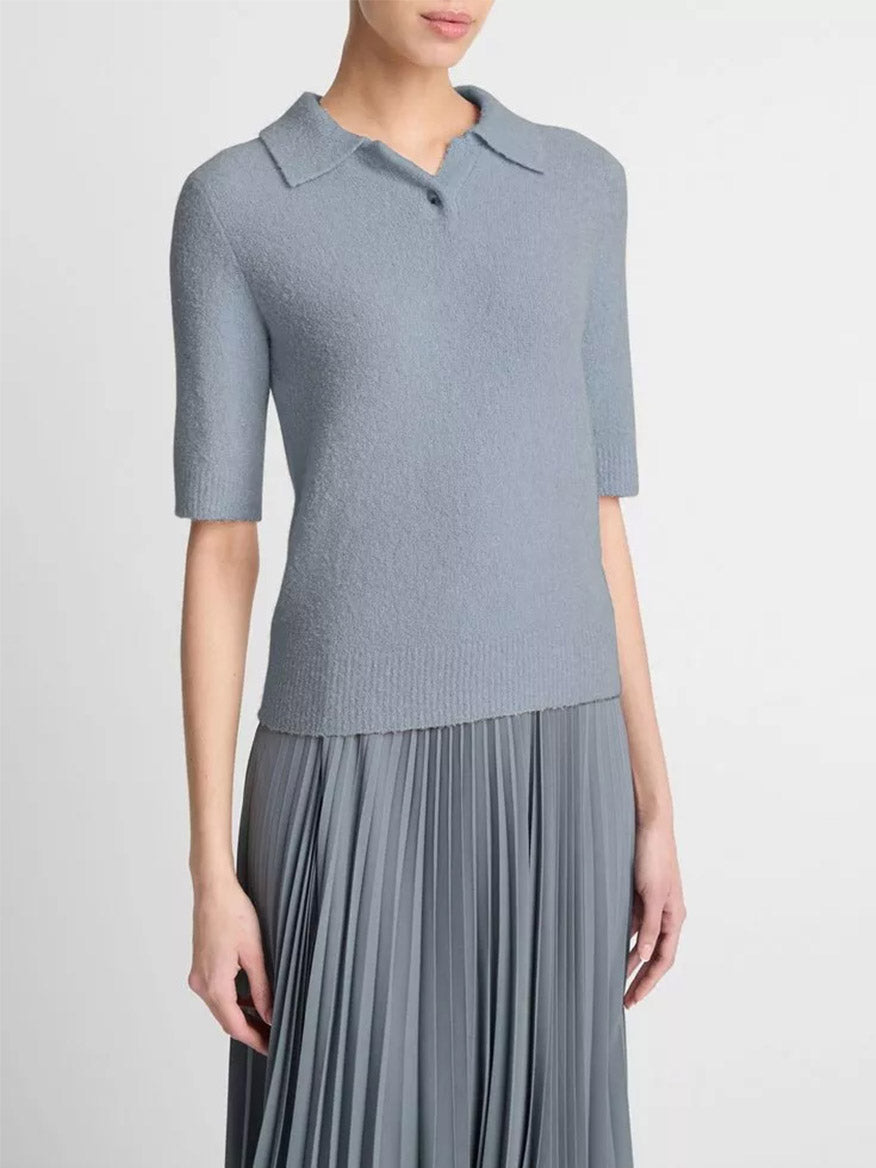 A person wearing the Vince Soft Bouclé Silk-Blend Polo Sweater in Lake Stone, a grey short-sleeve sweater with a collar, paired with a matching pleated skirt, shown from the shoulders to the hips against a plain background.