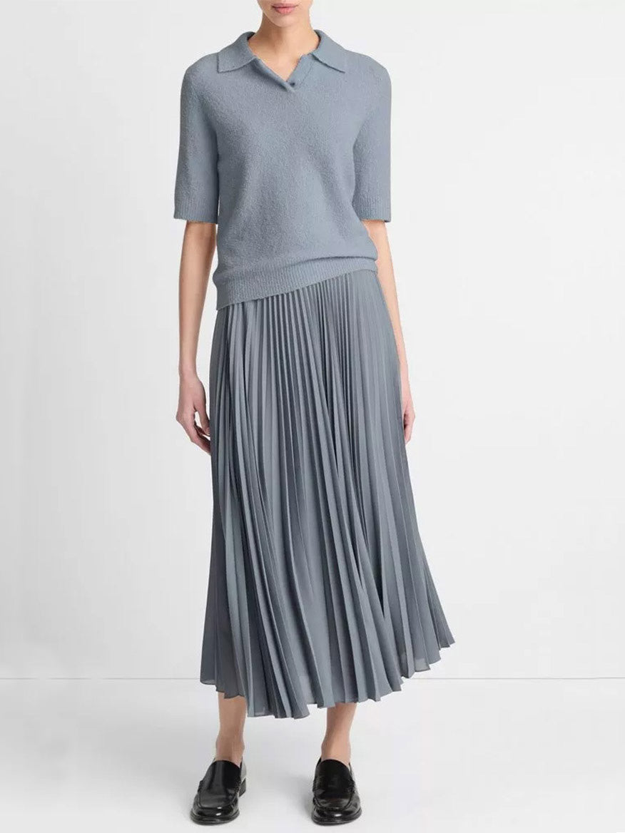 A person wearing the Vince Soft Bouclé Silk-Blend Polo Sweater in Lake Stone, paired with a pleated midi skirt and black loafers.