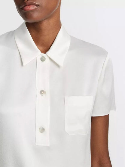 Close-up of a person wearing a Vince Silk Short-Sleeve Polo Shirt in Off-White with a collar and a front pocket.