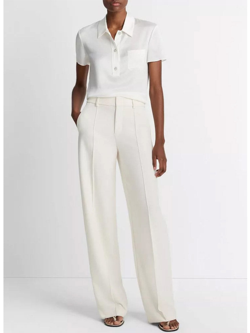 A person modeling a white short-sleeve Vince Silk Polo Shirt in Off-White with button-front closure, paired with light-colored high-waisted trousers.