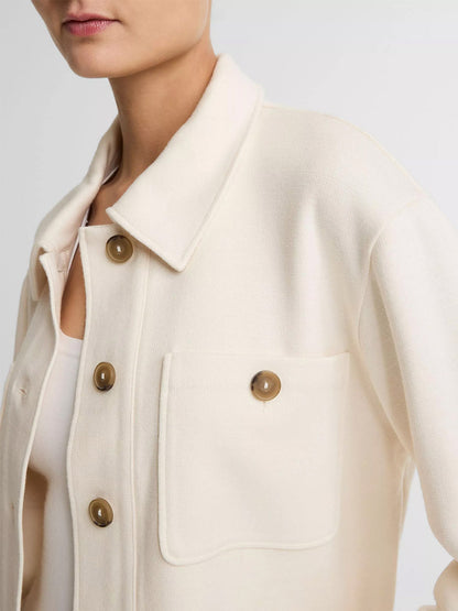 Someone wearing the Vince Ponte Knit Jacket in Off-White, featuring large brown buttons and a front pocket—a stylish transitional layer for cooler days, shown from shoulders to waist.